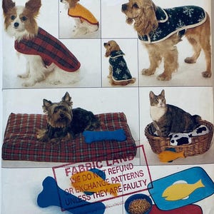 May include: A variety of pet accessories and clothing are shown, including dog coats, beds, and toys. The dog coats feature plaid and snowflake patterns. A cat sits in a wicker basket with a cow-print cushion. There are also bone and fish-shaped toys.