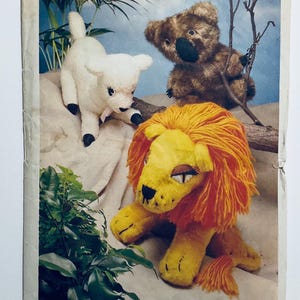 May include: A vintage image featuring three plush animal toys: a white lamb with black hooves, a brown koala, and a yellow lion with an orange mane. The toys are set against a backdrop of greenery and a light blue background.