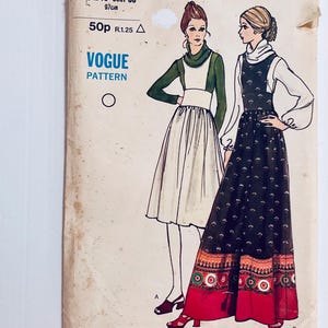 May include: Vintage Vogue Pattern showing illustrations of two dresses. One is a long, black patterned dress with a red and orange border. The other is a white dress with a green top. The pattern is on a worn, off-white background.