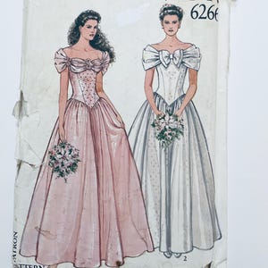 Może przedstawiać: Wzór do szycia w stylu vintage z dwiema ilustracjami sukni wieczorowych. Jedna jest jasnoróżowa z dekoltem w kształcie serca i rozkloszowaną spódnicą. Druga jest biała z dekoltem w kokardę i rozkloszowaną spódnicą. Oba modele trzymają bukiety.