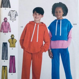 Puede incluir: Un patrón de costura con ilustraciones de sudaderas con capucha y pantalones de chándal para niños en varios colores. La imagen muestra a un niño con una sudadera con capucha y un pantalón de chándal naranja, y a una niña con una sudadera con capucha azul y rosa con un pantalón de chándal azul.
