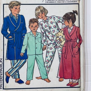 May include: Vintage pajama pattern featuring illustrations of children in various sleepwear styles. The designs include a blue robe with striped pajamas, a light green pajama set, floral pajamas, and a red robe with polka dot pajamas.