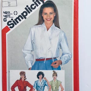May include: A Simplicity sewing pattern for a white blouse with a wrap style neckline and long sleeves. The pattern includes instructions for making the blouse in three different sizes. The pattern also includes a picture of a model wearing the blouse.