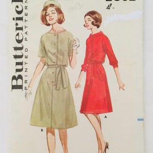 May include: Vintage Butterick printed sewing pattern with illustrations of two dresses. One is light green with short sleeves and buttons, the other is red with three-quarter sleeves and a tie waist. The pattern includes the text "Butterick Printed Pattern".