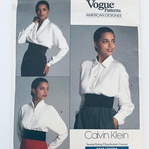 Könnte beinhalten: Eine Vogue Patterns American Designer Schnittmusterhülle von Calvin Klein mit drei Varianten einer langärmeligen weißen Bluse mit breitem schwarzem Taillenbund. Der Text enthält Vogue Patterns, American Designer und Calvin Klein.