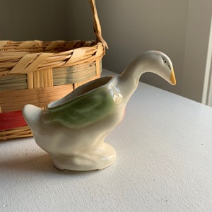 Könnte beinhalten: Eine Keramik-Gänsefigur mit grüner und rosa Glasur. Die Gans hat einen langen Hals und einen kleinen Schnabel. Es ist ein Blumentopf im Vintage-Stil.