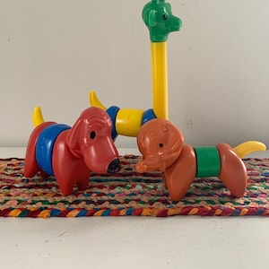 May include: Colorful plastic toy animals, including a red dog, an orange elephant, and a giraffe. The dog has blue and red sections, the elephant has a green section, and the giraffe has a yellow neck and green head. The toys are on a multi-colored braided mat.