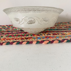 May include: A frosted glass light fixture shade with a decorative leaf and vine pattern. The shade is bowl-shaped and sits on a colorful braided mat. The shade is made of clear glass with a frosted finish.