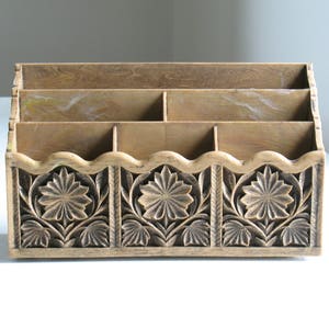 Peut inclure: Un organiseur de bureau en bois avec cinq compartiments et un motif floral sculpté. L'organisateur est brun clair avec un motif sculpté brun foncé.