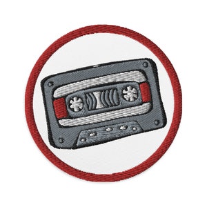 May include: A red and white embroidered patch with a vintage cassette tape design. The tape is gray with a red stripe and is angled slightly.