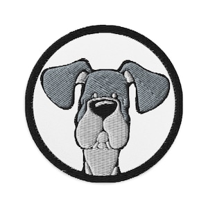 Può includere: Una toppa ricamata in bianco e nero di un cane dei cartoni animati con grandi orecchie e un'espressione sciocca. Il cane è in un cerchio con un contorno nero.