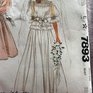 May include: An illustration of a vintage wedding dress pattern. The bride is shown in a white gown with a high neckline, puff sleeves, and a bow at the waist. She holds a bouquet of white flowers and wears a veil. The pattern is labeled "7893" and "Miss Size 10".