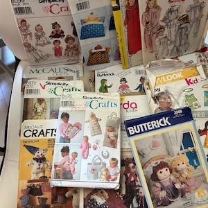 May include: A collection of various sewing patterns for dolls and children's clothing, featuring brands such as Simplicity, Butterick, and McCall's. The envelopes display illustrations of finished garments, stuffed toys, and dolls with printed text and barcodes.