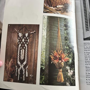 Op de afbeelding: Een pagina uit een knutselboek getiteld "beehive book no. 413" met macram&eacute;-projecten. De pagina bevat afbeeldingen van een wandkleed van drijfhout, een kussen en een hangende plantenbak met gedroogde bloemen. De tekst bevat de inhoud van het boek.