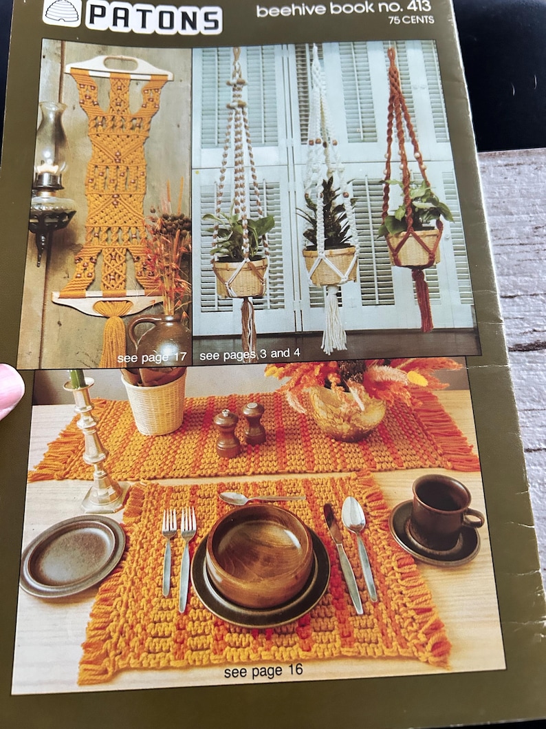Op de afbeelding: Een afbeelding uit een vintage knutselboek met macram&eacute; plantenhangers, een wandkleed en een tafelsetting. De tafelsetting omvat een placemat, bord, kom, bestek en een kop en schotel. De tekst "PATONS beehive book no. 413 75 CENTS" is zichtbaar.