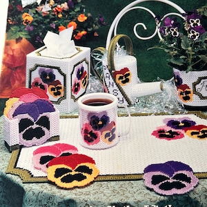 Puede incluir: Colección de artículos hechos a mano con el tema de las flores de pensamiento. Incluye una funda para caja de pañuelos, una taza, posavasos y una maceta, todos con fondo blanco y diseños coloridos de pensamientos. El texto "Pretty Pansies" es visible.