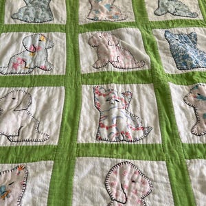 May include: A quilted blanket featuring a grid of white squares separated by bright green fabric strips. Each white square contains a fabric applique of a dog or cat in various floral and patterned prints, outlined with black decorative stitching.