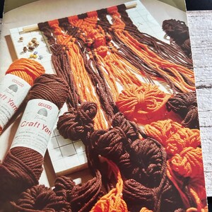 Op de afbeelding: Een vintage boekomslag getiteld "Macram&eacute; in colour" met een macram&eacute;project in uitvoering. Het project gebruikt bruin en oranje garen, met spoelen bruin en oranje handwerkgaren op de voorgrond. De omslag is groen en wit.