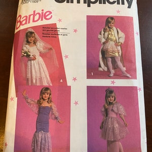 Puede incluir: Un patrón de costura Simplicity para disfraces de muñeca Barbie. El patrón incluye cuatro disfraces diferentes: un vestido de novia blanco, un vestido morado, un vestido rosa con capa y un abrigo blanco con falda dorada. El patrón se titula "Barbie" e incluye el texto "Rosettes bouffantes et gants montants inclus."