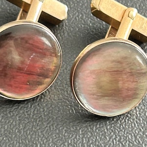 May include: A pair of gold-toned cufflinks with iridescent, round faces. The faces display a mix of red, brown, and gold hues. The cufflinks have a classic, rectangular bar design for securing them to a shirt cuff.