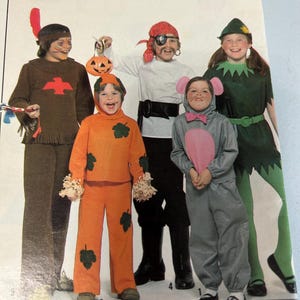 May include: A vintage sewing pattern showing children in Halloween costumes. The costumes include a Native American, a pumpkin, a pirate, a mouse, and a forest sprite. The costumes are in brown, orange, grey, green, and white.