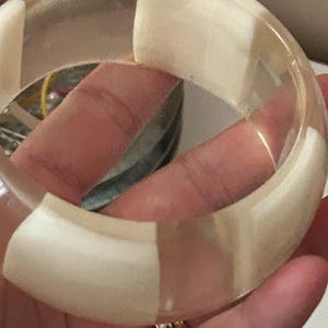 May include: A thick, circular bangle bracelet featuring alternating segments of clear, transparent material and opaque, off-white, matte-textured sections. The design creates a repeating pattern around the entire circumference of the jewelry piece.