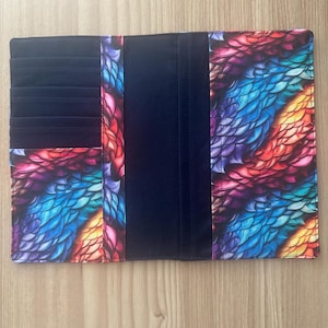 May include: A rectangular fabric wallet or checkbook cover featuring a vibrant, multi-colored scale pattern in shades of blue, purple, pink, and orange. The interior includes solid black fabric sections with multiple horizontal card slots.