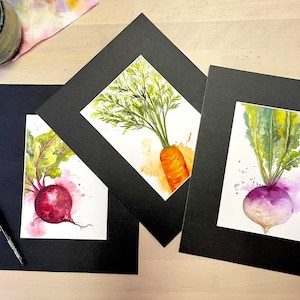May include: Three watercolor paintings of vegetables framed in black mats. The paintings feature a beet, a carrot, and a turnip.
