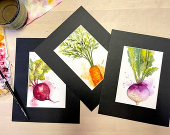 May include: Three watercolor paintings of vegetables framed in black mats. The paintings feature a beet, a carrot, and a turnip.