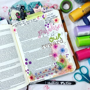 Puede incluir: Biblia abierta con ilustraciones florales coloridas y texto manuscrito, incluyendo las palabras "Paradise is our reward". Tambi&eacute;n se ven suministros adicionales como marcadores, cinta washi y tijeras.