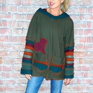 May include: An olive green hooded sweatshirt with a burgundy heart applique and two front pockets. The sleeves have striped accents in teal, orange, and burgundy. The sweatshirt is paired with blue jeans and black and white sneakers.