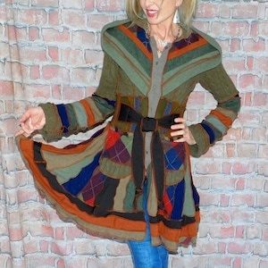 May include: A colorful patchwork coat with a black belt, featuring a mix of orange, green, blue, and purple panels. The coat has long sleeves and a unique design. The person is wearing blue jeans and black and white sneakers.