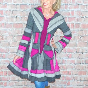 May include: A gray, pink, and purple patchwork coat with a hood. The coat features a button-up front, pockets, and striped sleeves. The coat is knee-length and has a flared skirt. The model is wearing blue jeans and brown boots.