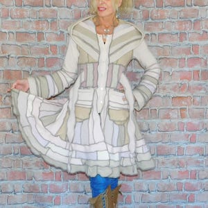 May include: A long, white, patchwork coat with a hood. The coat has a layered, ruffled hem and a button closure. The coat is made of different fabrics and textures, including knit, woven, and felt.