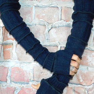 May include: A pair of dark navy blue arm warmers featuring a ribbed knit texture and horizontal seam detailing. These long, fingerless sleeves extend from the upper arm to the knuckles, providing full coverage with an open thumb hole design.