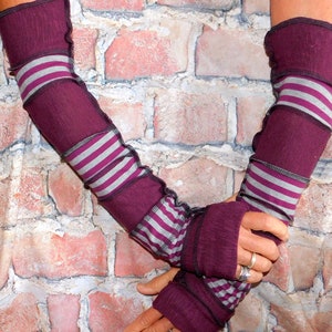May include: A pair of long, striped arm warmers in shades of purple and gray. The arm warmers are made of a soft, stretchy fabric and have a ruffled edge.