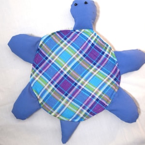 Puede incluir: Una tortuga de tela azul con un caparazón a cuadros. La tortuga tiene dos ojos negros y está hecha de tela suave.