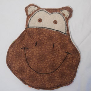 May include: A brown fabric hippopotamus with a smiling face. The hippo has two black eyes and a black stitched smile. The fabric is brown with a white polka dot pattern.
