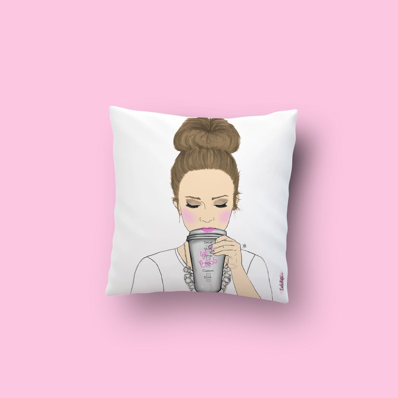 May include: White throw pillow with a drawing of a woman with a bun in her hair, wearing a white shirt and a necklace, holding a coffee cup that says "Good Vibes, Badass, Coffee, Confidence, Dreams, Goals".