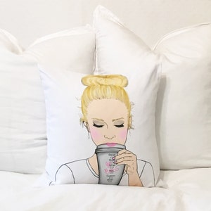 May include: A white pillow with a drawing of a woman with blonde hair in a bun, wearing a white shirt and drinking from a coffee cup. The coffee cup has the words "Decaf, Shots, Syrup, Milk, Cream, Custom Drink" written on it.