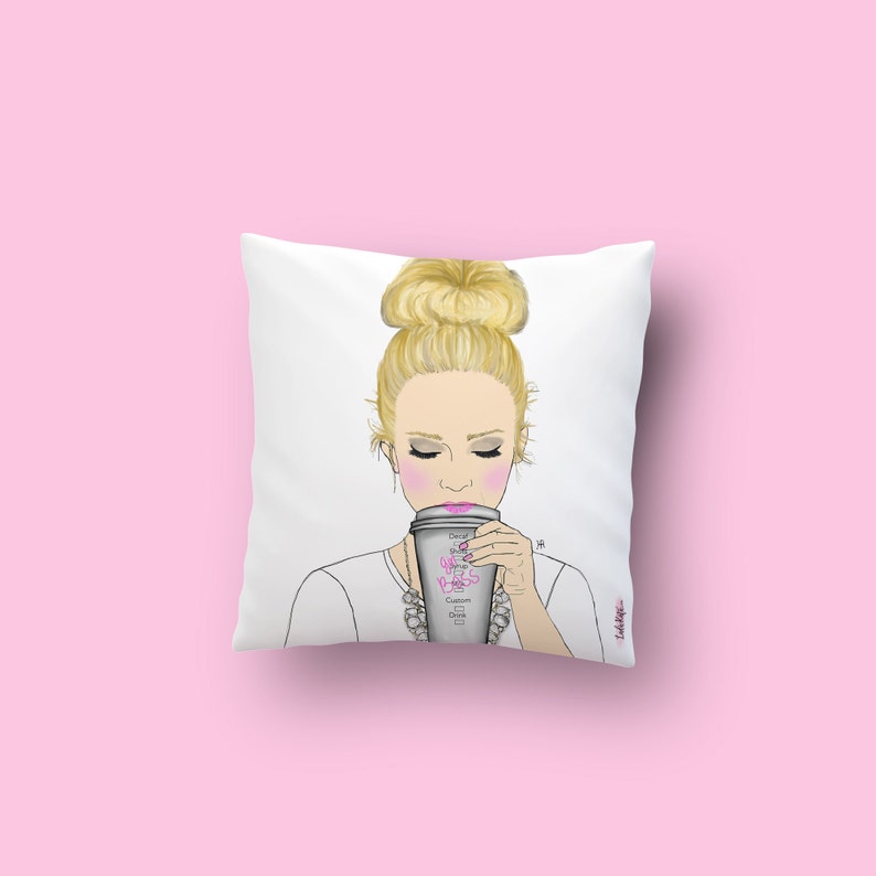 May include: White throw pillow with a drawing of a woman with blonde hair in a bun, wearing a white shirt and a pearl necklace, holding a coffee cup that says "Girl Boss" in pink lettering.