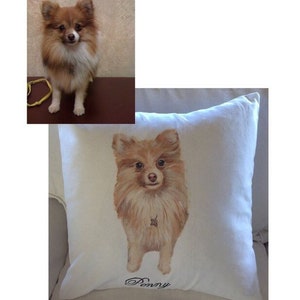 May include: A white pillow with a hand-painted image of a brown and white Pomeranian dog. The dog is looking at the camera and the pillow has the name "Penny" embroidered on it.