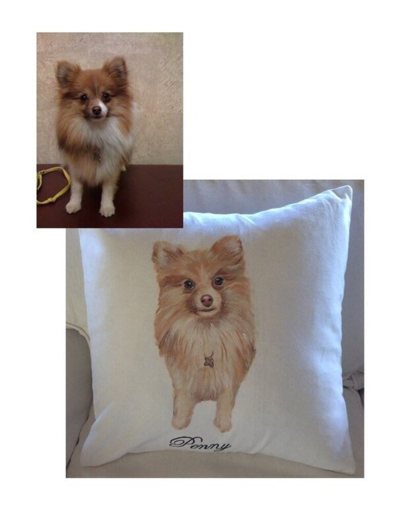 May include: A white pillow with a hand-painted image of a brown and white Pomeranian dog. The dog is looking at the camera and the pillow has the name "Penny" embroidered on it.