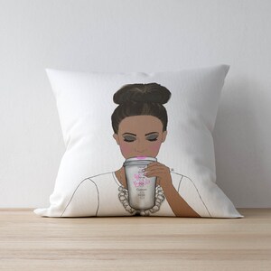 May include: White throw pillow with a graphic of a woman with a bun in her hair, wearing a white shirt and a pearl necklace, holding a coffee cup with the text "Don't Be A Princess, Be A Queen" on it.