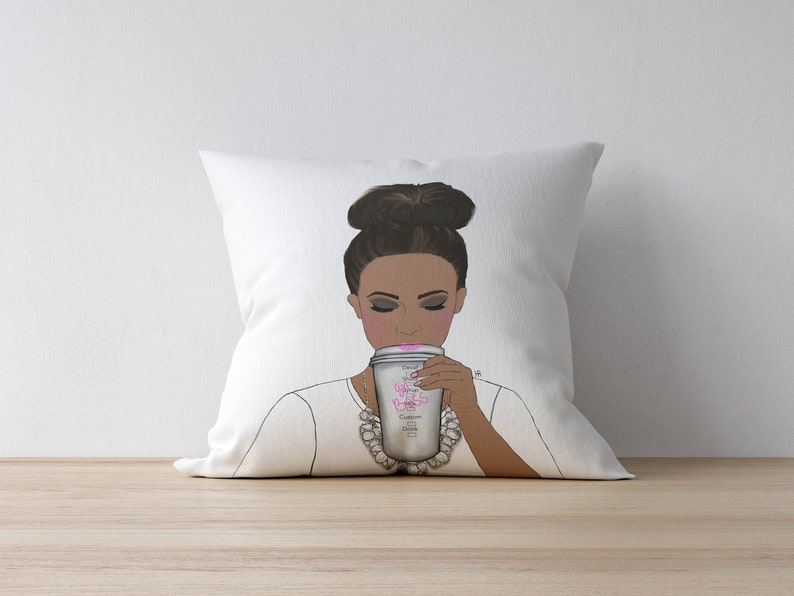May include: White throw pillow with a graphic of a woman with a bun in her hair, wearing a white shirt and a pearl necklace, holding a coffee cup with the text "Don't Be A Princess, Be A Queen" on it.