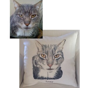 May include: A white pillow with a hand-painted portrait of a gray tabby cat with yellow eyes. The cat's name, "Loxy", is written in black lettering below the portrait.