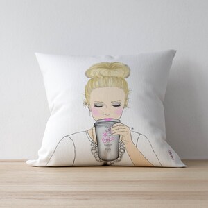 May include: White throw pillow with a drawing of a woman with blonde hair in a bun, wearing a white shirt and a silver necklace, holding a coffee cup with the text "Don't smile, it's just coffee" printed on it.