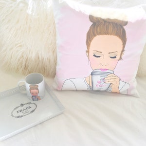 May include: A white pillow with a pink background featuring an illustration of a woman with brown hair in a bun, wearing a white shirt and a necklace, drinking from a white coffee cup with pink writing that says "Get Your Boss On".