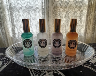 Peut inclure: Quatre flacons en verre avec des bouchons dorés et des étiquettes indiquant "The Sanctum of Light" et différents parfums : "Mythic & Brew", "Arctic White Magic", "Lunar Meditation" et "Solar Cleansing".