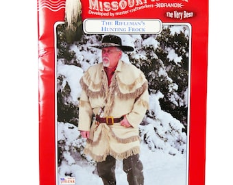 May include: A vintage-style hunting frock pattern from Missouri River Brand. The pattern features a man wearing a white frock with fringe trim, a brown belt, and a black hat. The pattern is set against a snowy winter background.